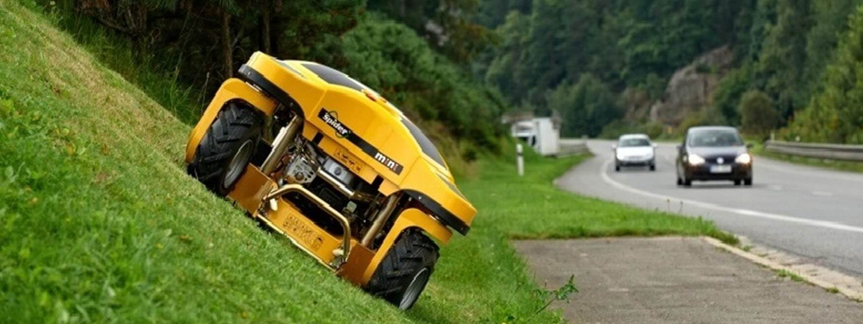 Žlutá dálkově řízená sekačka Spider při sekání travnatého svahu u silnice